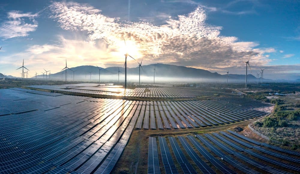 Aerial view of a large solar farm with wind turbines at sunrise